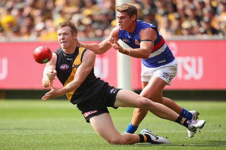 JACK RIEWOLDT of the Tigers handballs whilst being tackled by MICHAEL TALIA of the Bulldogs during the AFL match between the Richmond Tigers and the Western Bulldogs at MCG in Melbourne, Australia.