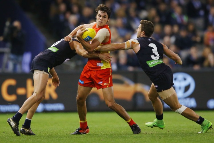 KADE KOLODJASHNIJ of the Suns gets tackled by Kade Simpson and Marc Murphy of the Blues during the AFL match between the Carlton Blues and the Gold Coast Suns at Etihad Stadium in Melbourne, Australia.