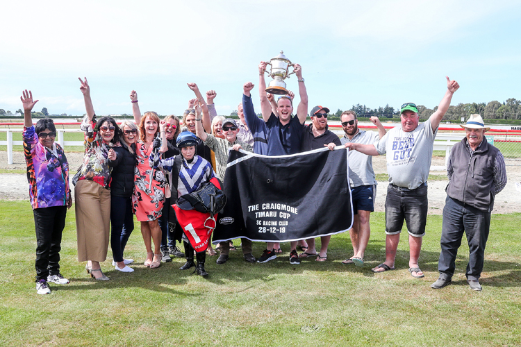 Jockey Sam Wynne poses with the connections of Who Dares Wins as they celebrate their victory at Timaru