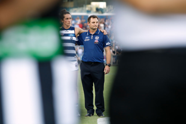 PAUL HOOD, Senior Coach of the Cats looks on during the national anthem during the NAB AFLW match between the Geelong Cats and the Collingwood Magpies at GMHBA Stadiumin Geelong, Australia. PAUL HOOD, Senior Coach of the Cats looks on during the national anthem during the NAB AFLW match between the Geelong Cats and the Collingwood Magpies at GMHBA Stadiumin Geelong, Australia.